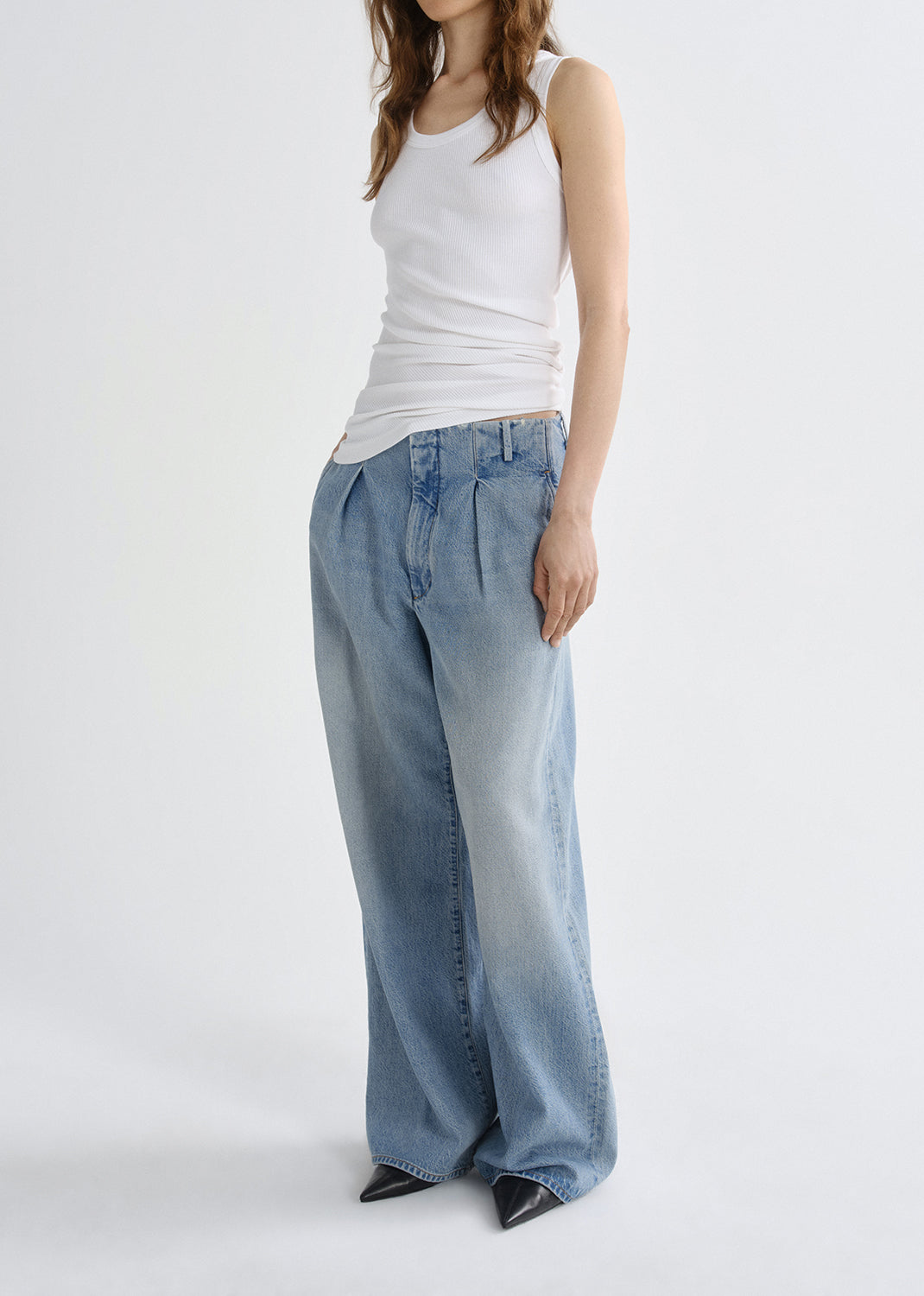 Person wearing a white tank top and light blue jeans on a grey background