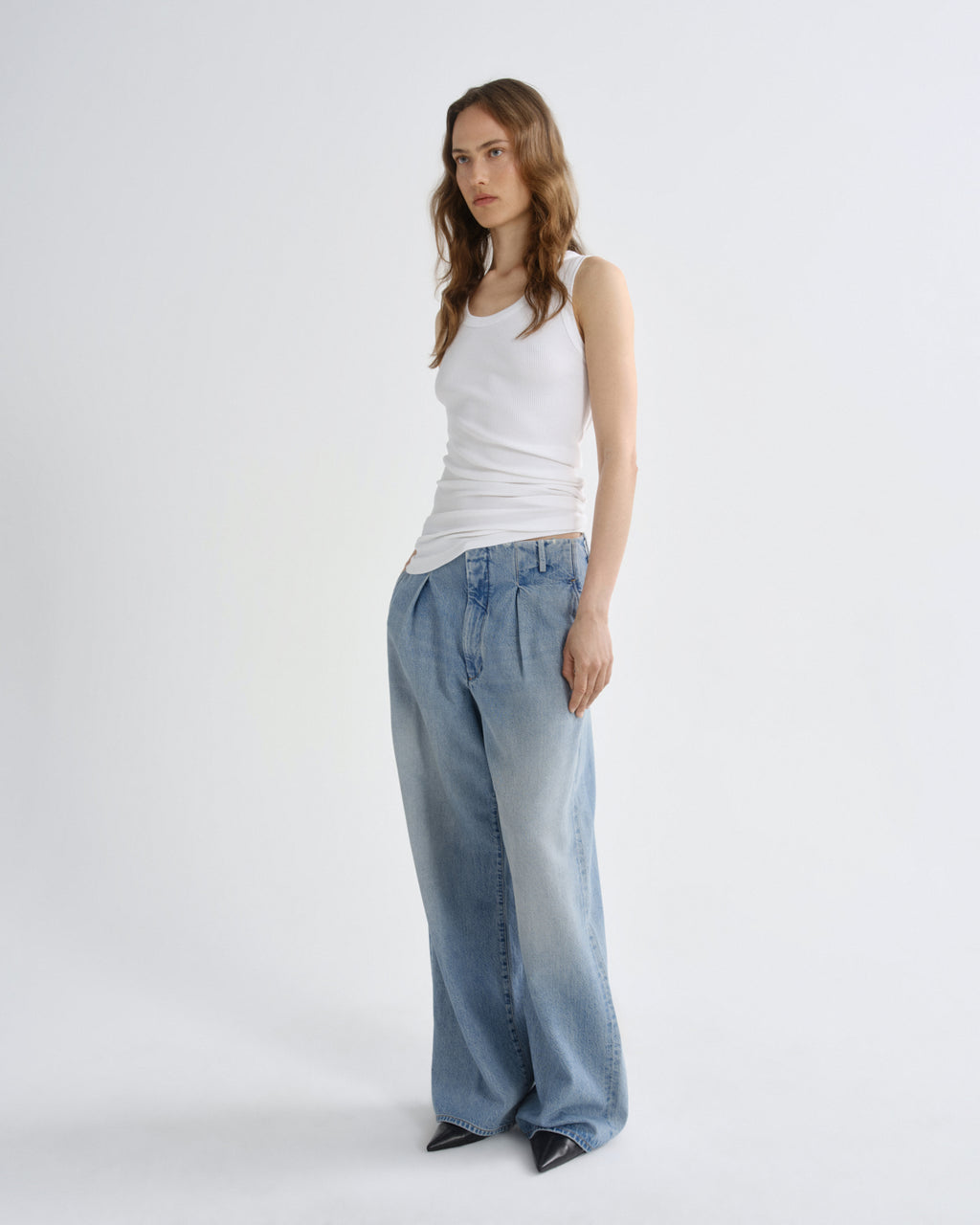 A woman modeling a white ribbed tank top and wide-leg light blue denim jeans against a plain white studio background.