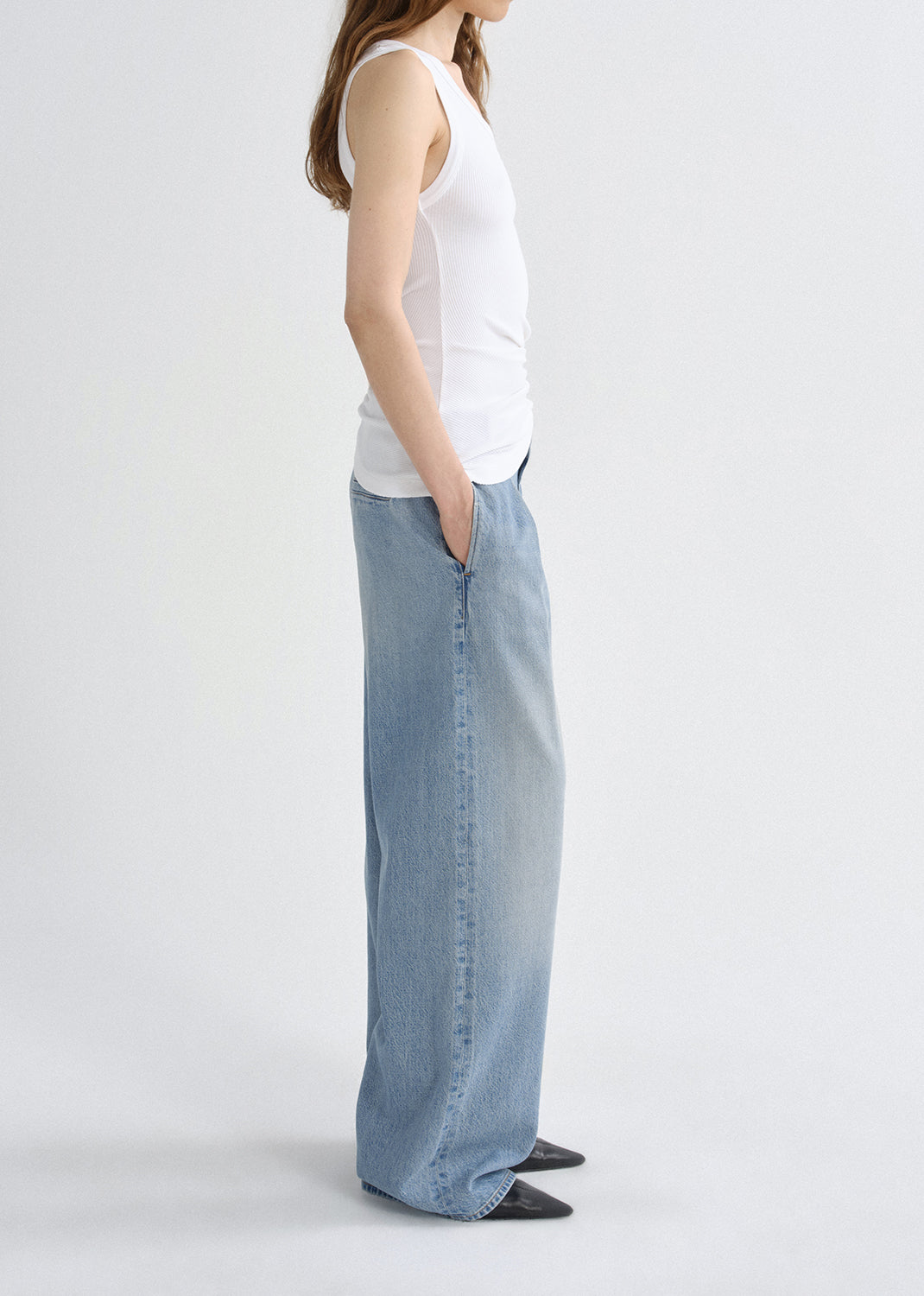 Person wearing a white tank top and light blue jeans on a grey background