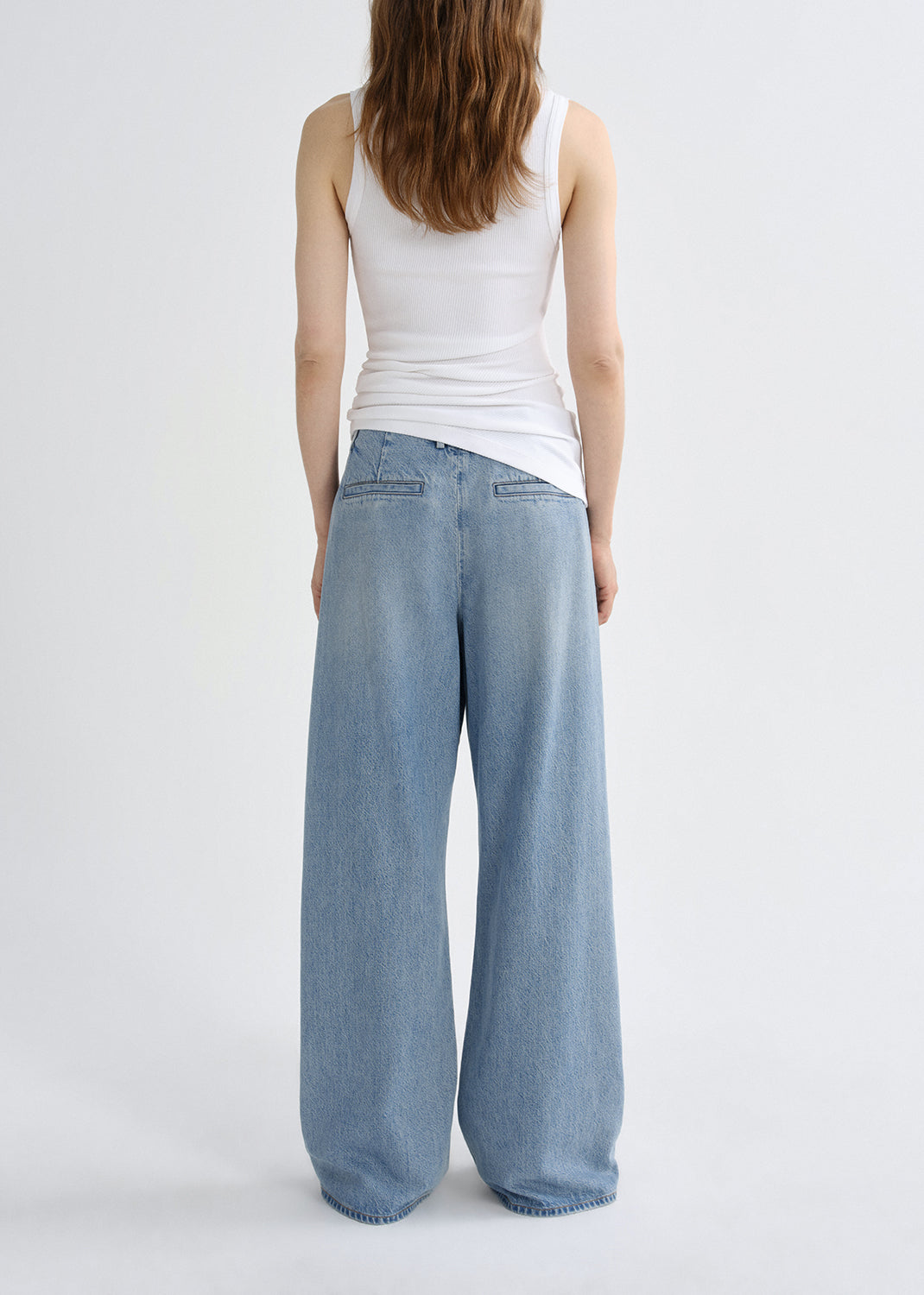 Person wearing light blue wide-leg jeans and a white tank top on a grey background