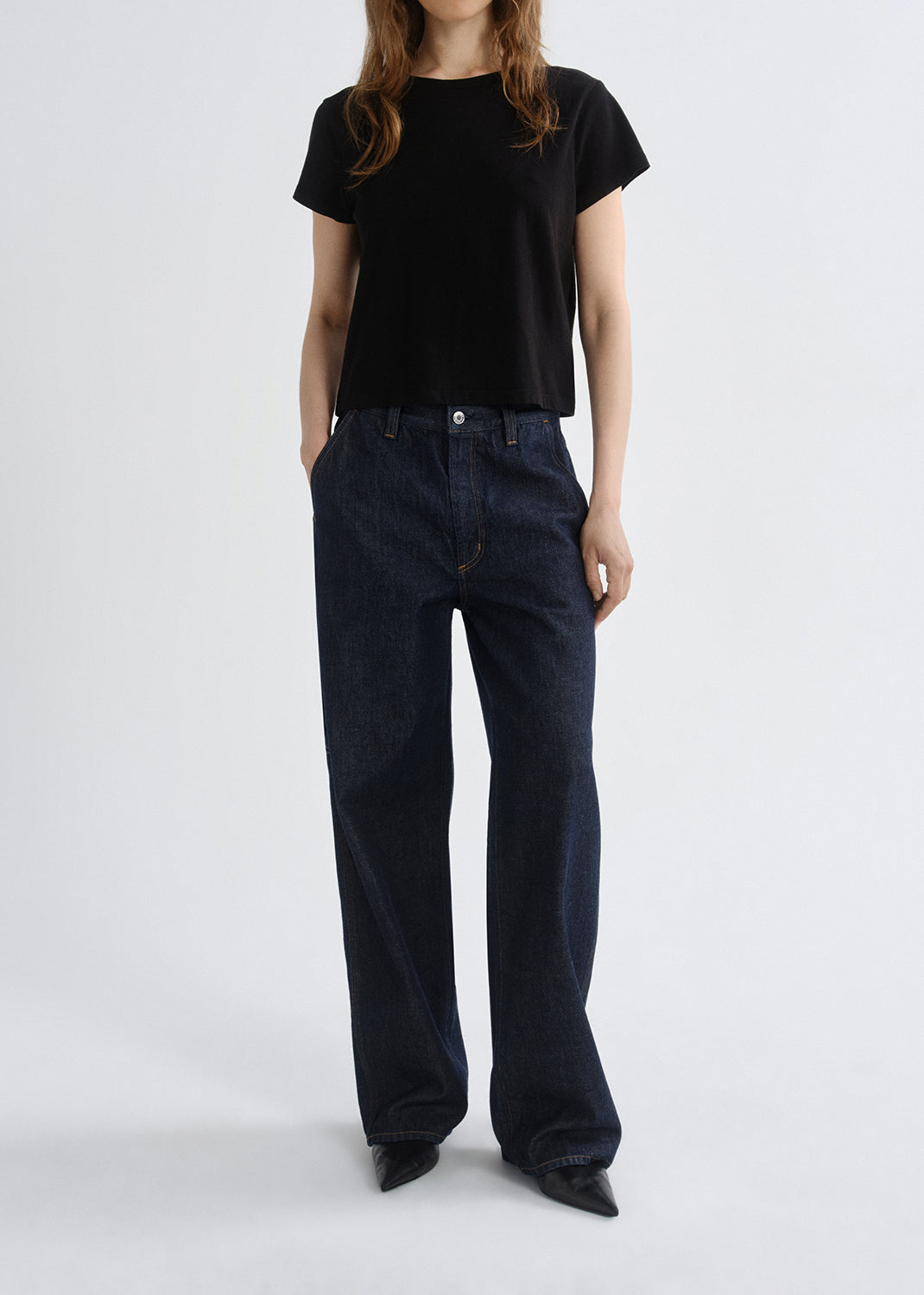 Person wearing a black t-shirt and dark blue jeans on a grey background