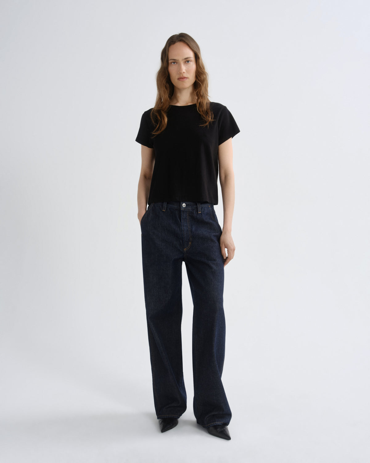 Person wearing a black t-shirt and dark blue jeans on a white background