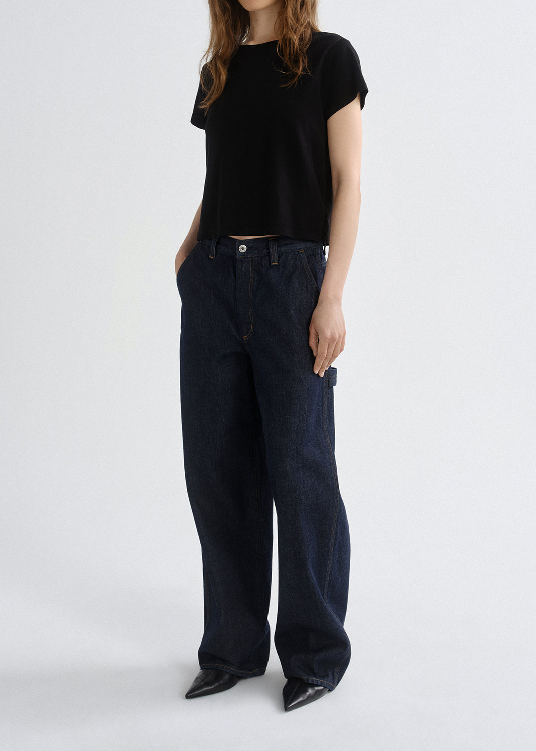 Person wearing a black t-shirt and dark blue jeans on a grey background