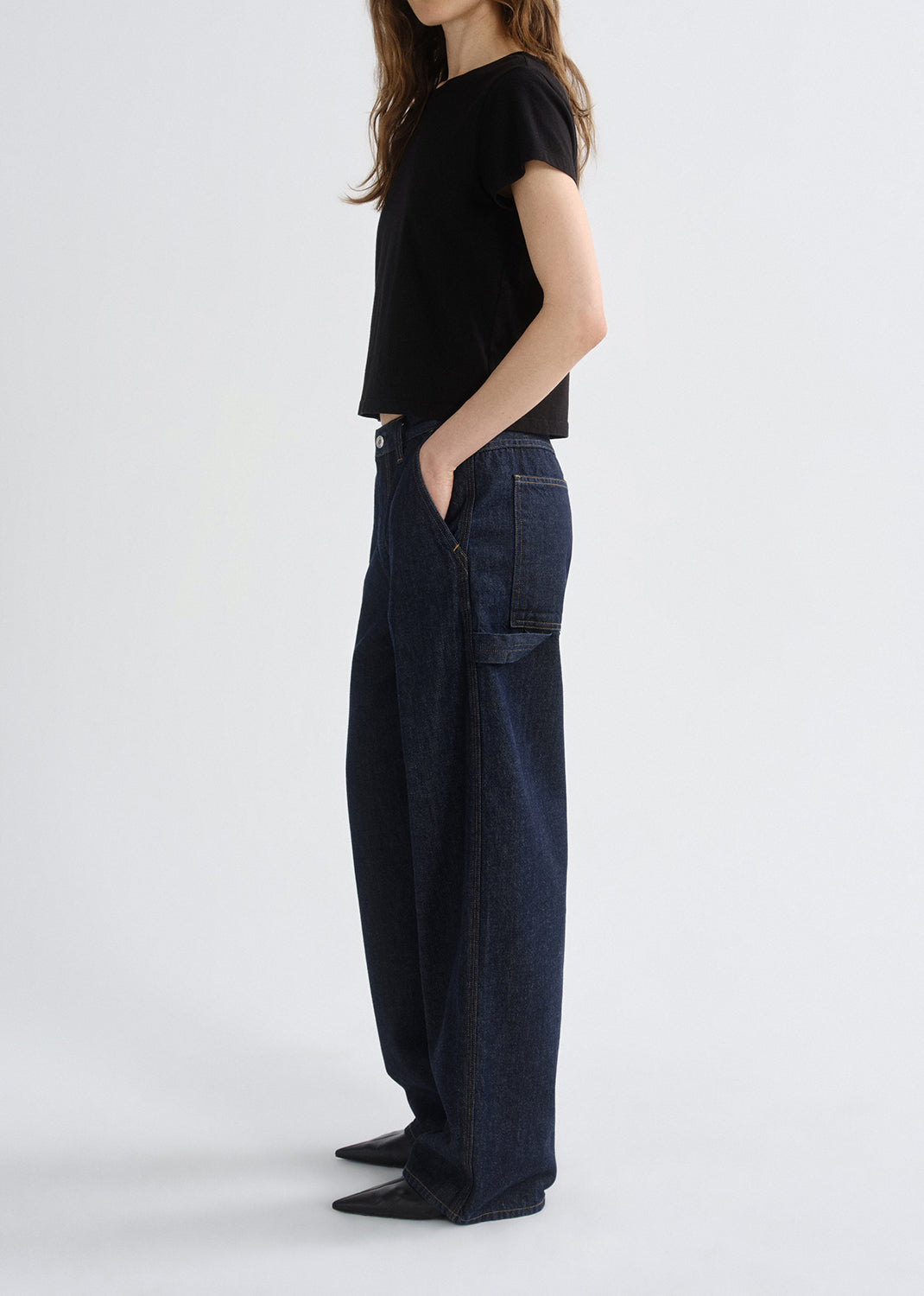 Person wearing a black top and dark blue jeans on a grey background