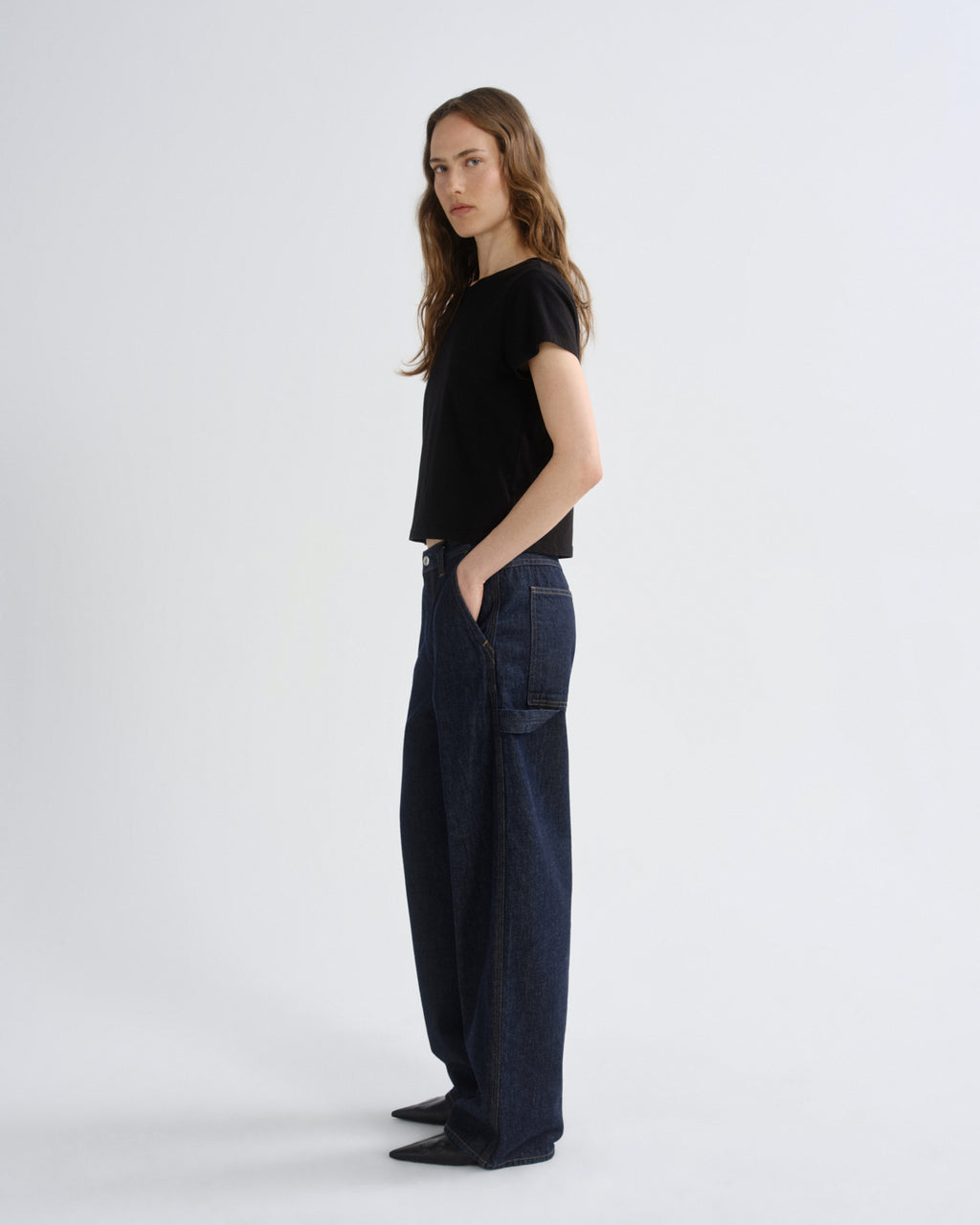 Woman wearing a black top and dark jeans on a white background