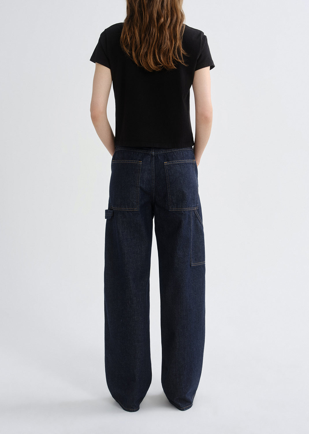 Person wearing dark blue jeans and a black t-shirt on a grey background