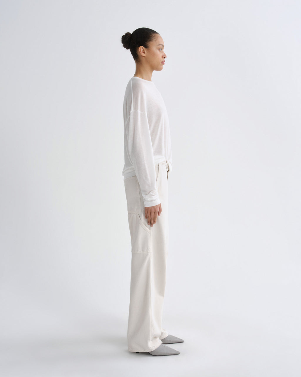 Person wearing a white long-sleeve top and cream pants on a white background