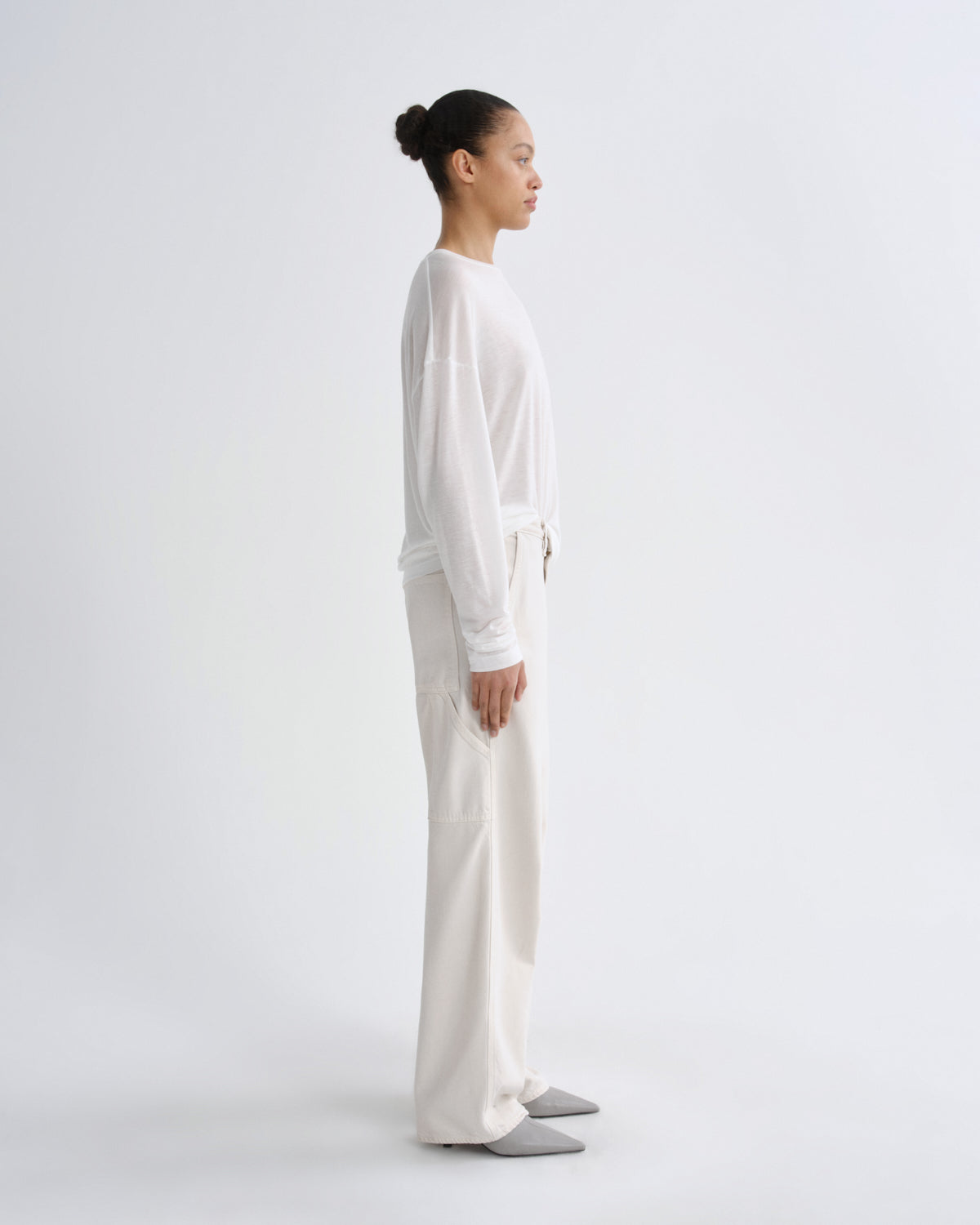 Person wearing a white long-sleeve top and cream pants on a white background