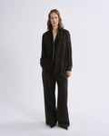 A model stands against a grey background wearing a dark brown long-sleeve button-front jacket with a relaxed, oversized fit and matching wide-leg trousers.
