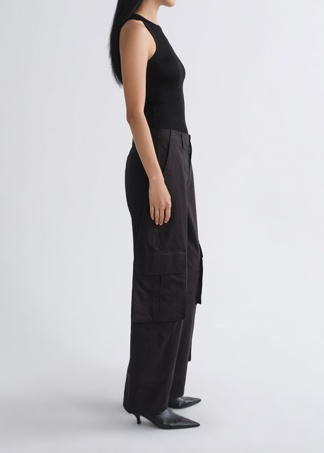 A model shown in profile wearing a black sleeveless top and black wide-leg cargo pants against a grey background.