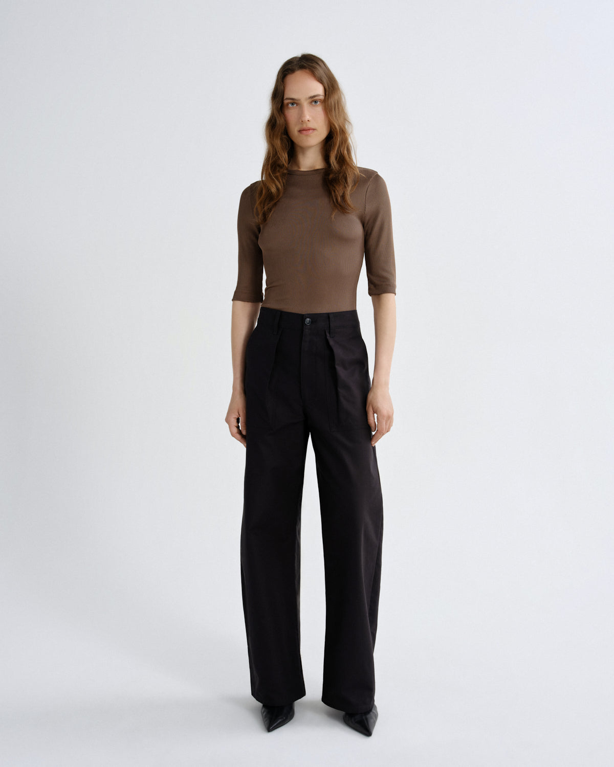 Woman wearing a brown top and black pants on a white background