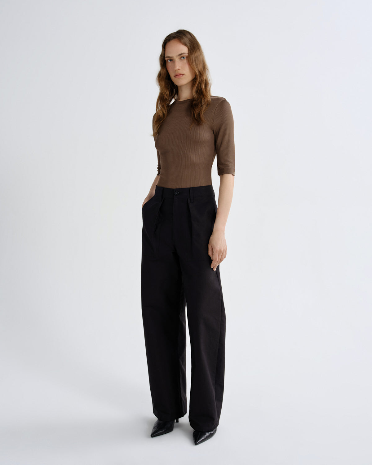 Woman wearing a brown top and black pants on a white background