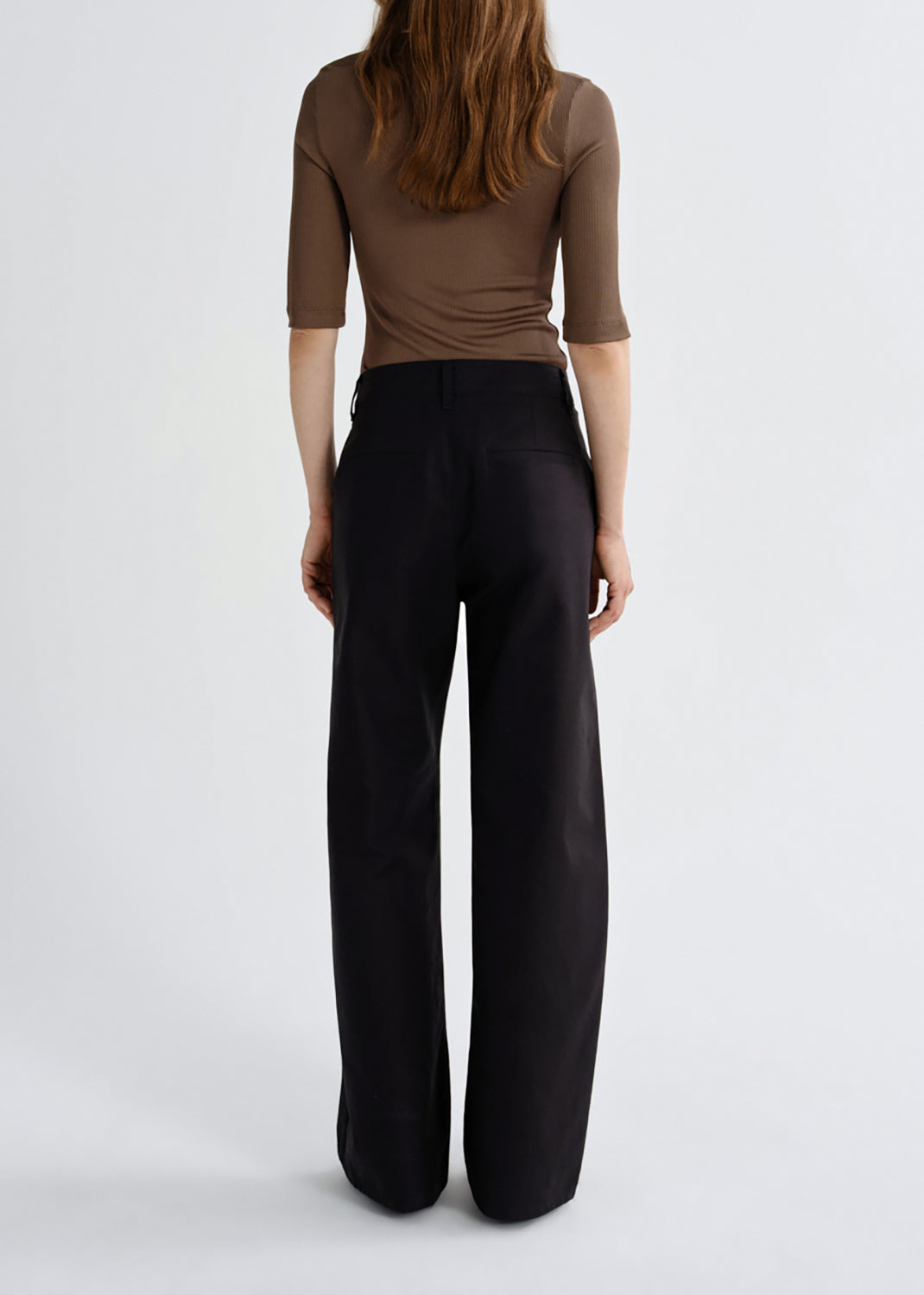 A model shown from the back wearing a brown short-sleeve top and black wide-leg trousers against a grey background.