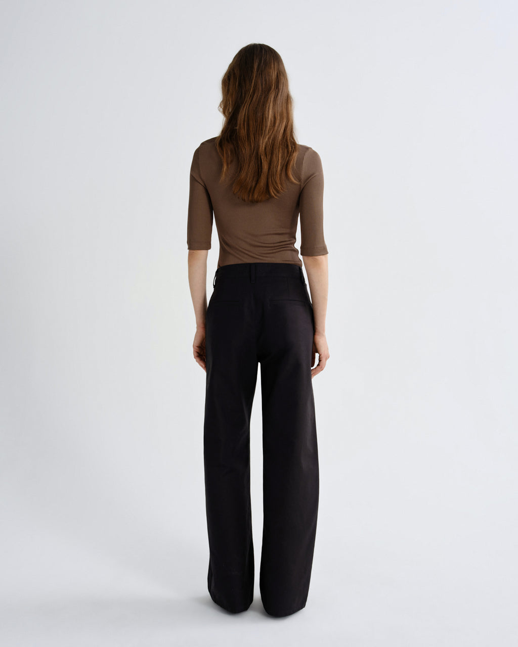 Woman wearing a brown top and black pants on a white background