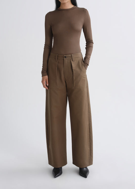 A model wearing a fitted long-sleeve brown top and matching wide-leg pleated trousers, paired with black pointed shoes, against a grey background.