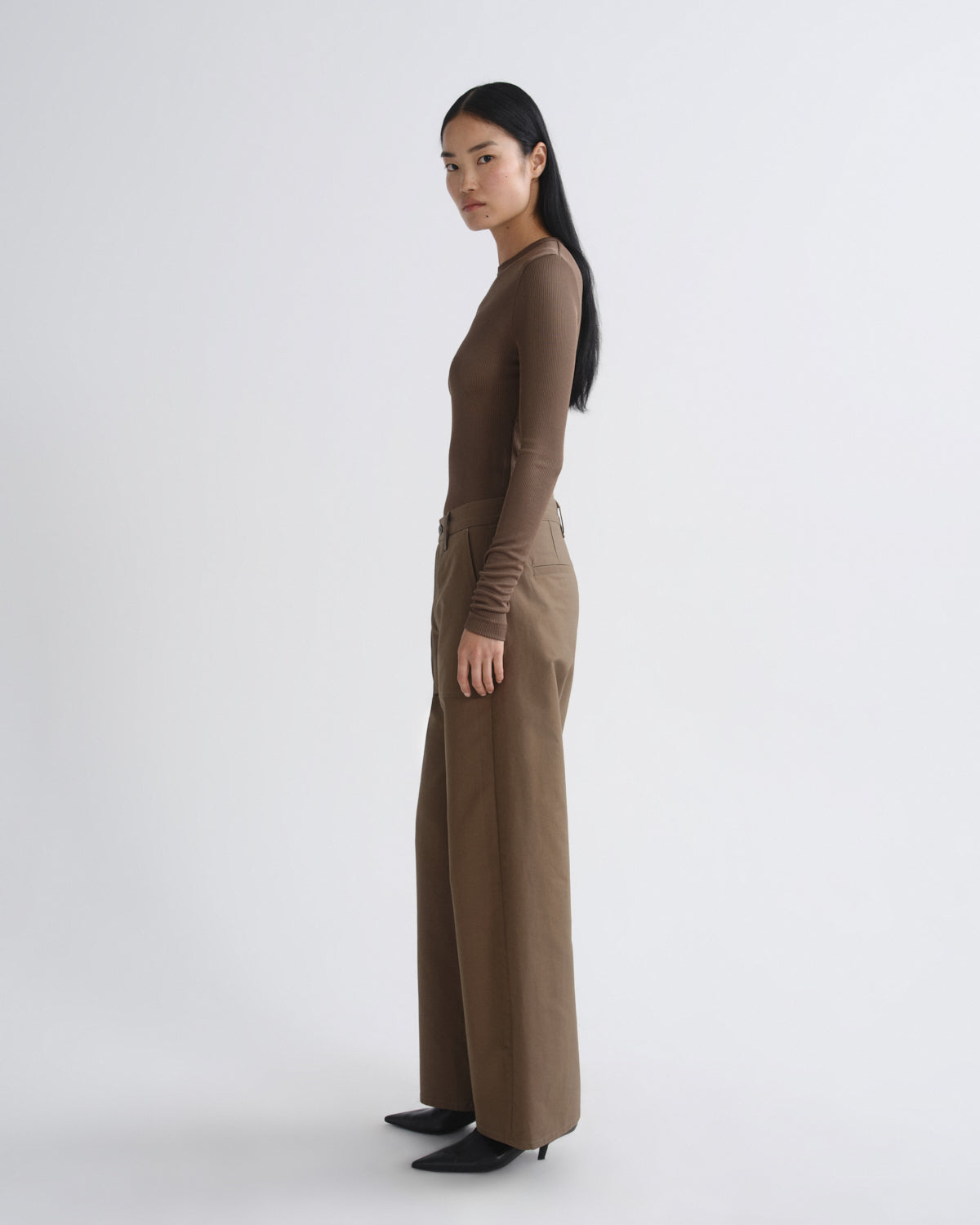 Woman wearing a brown long-sleeve top and beige wide-leg pants on a white background