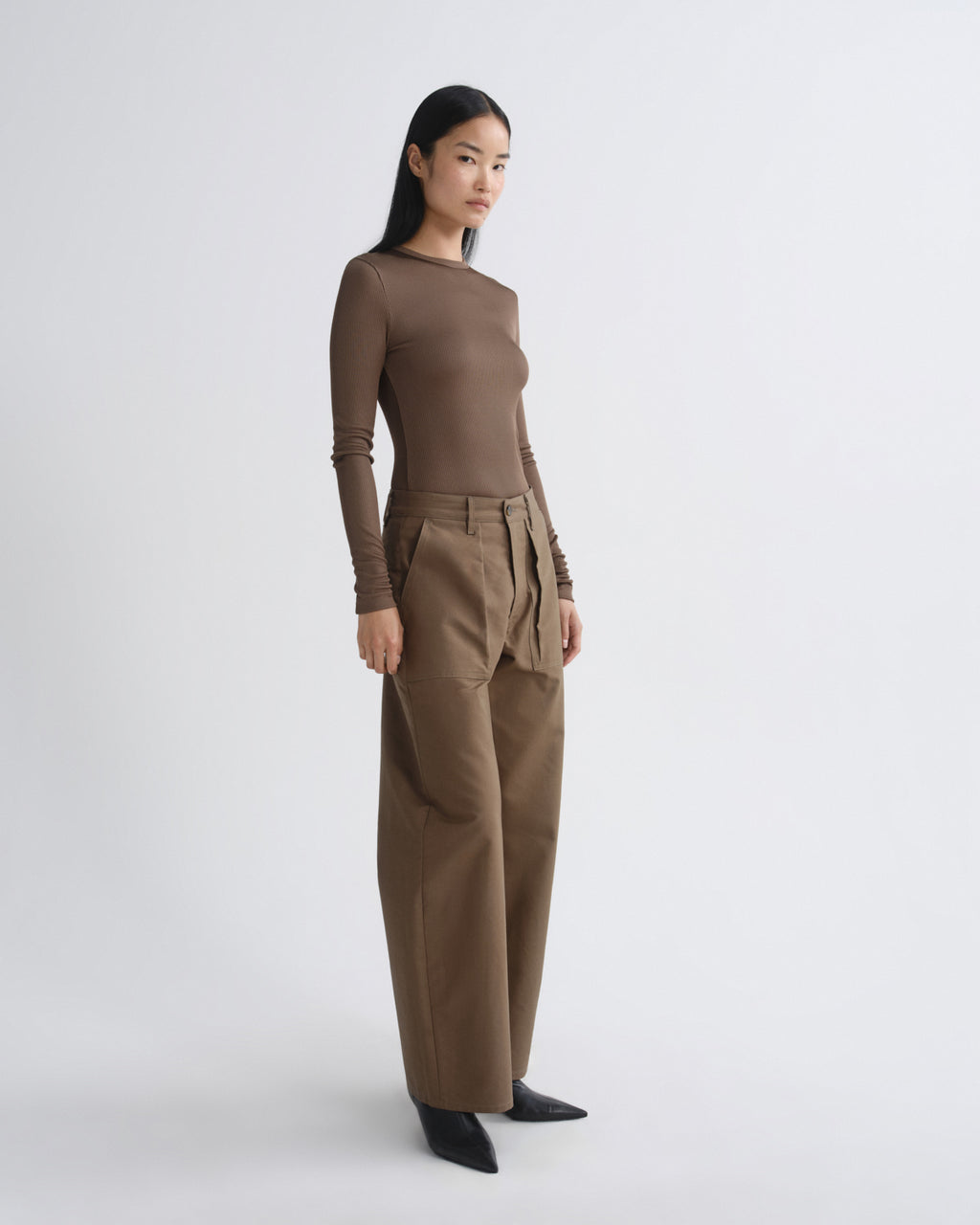 Woman wearing a brown long-sleeve top and beige pants on a white background