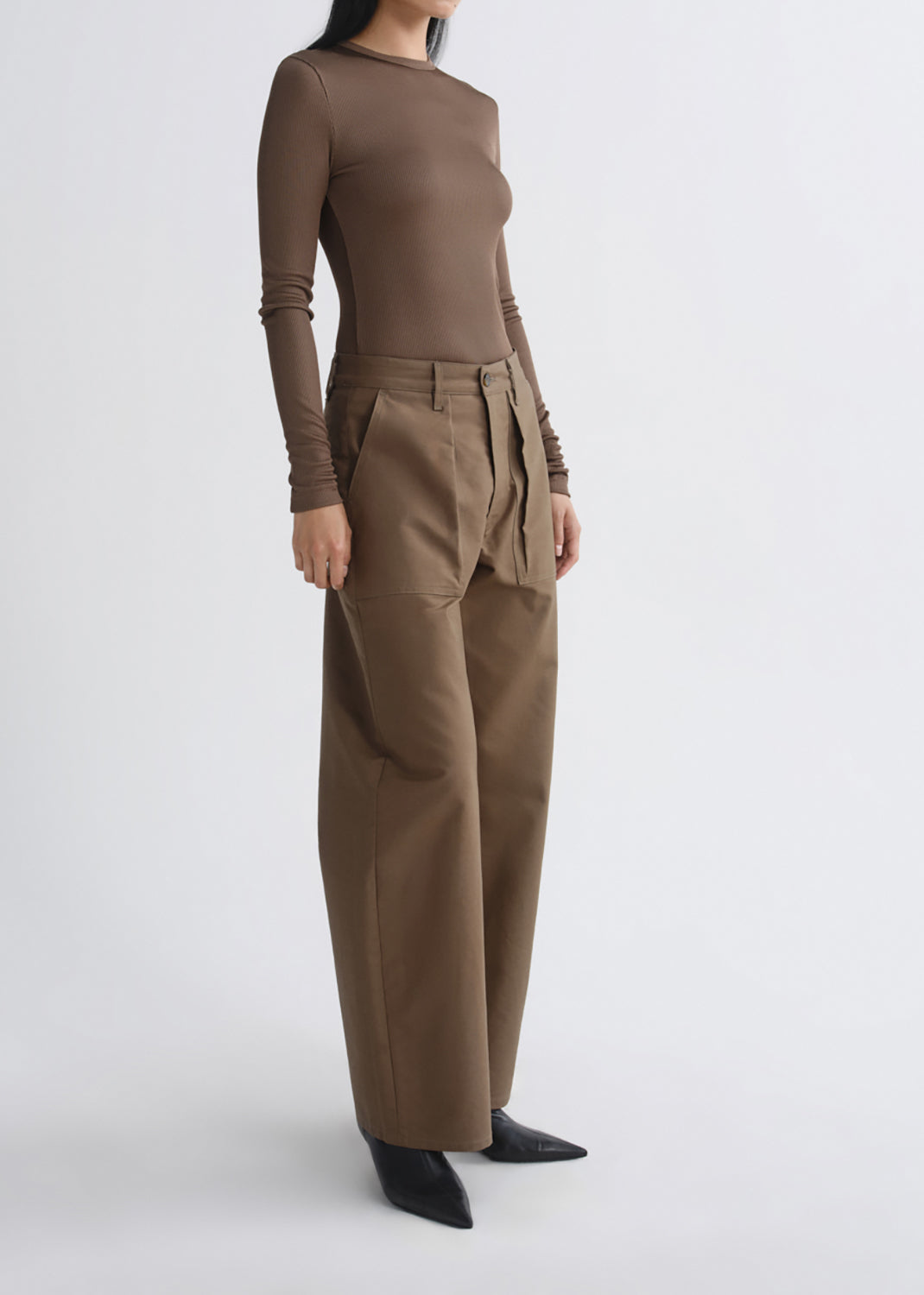 A model wearing a brown long-sleeve top and matching wide-leg trousers with a tie belt, paired with black pointed shoes, photographed against a grey background.