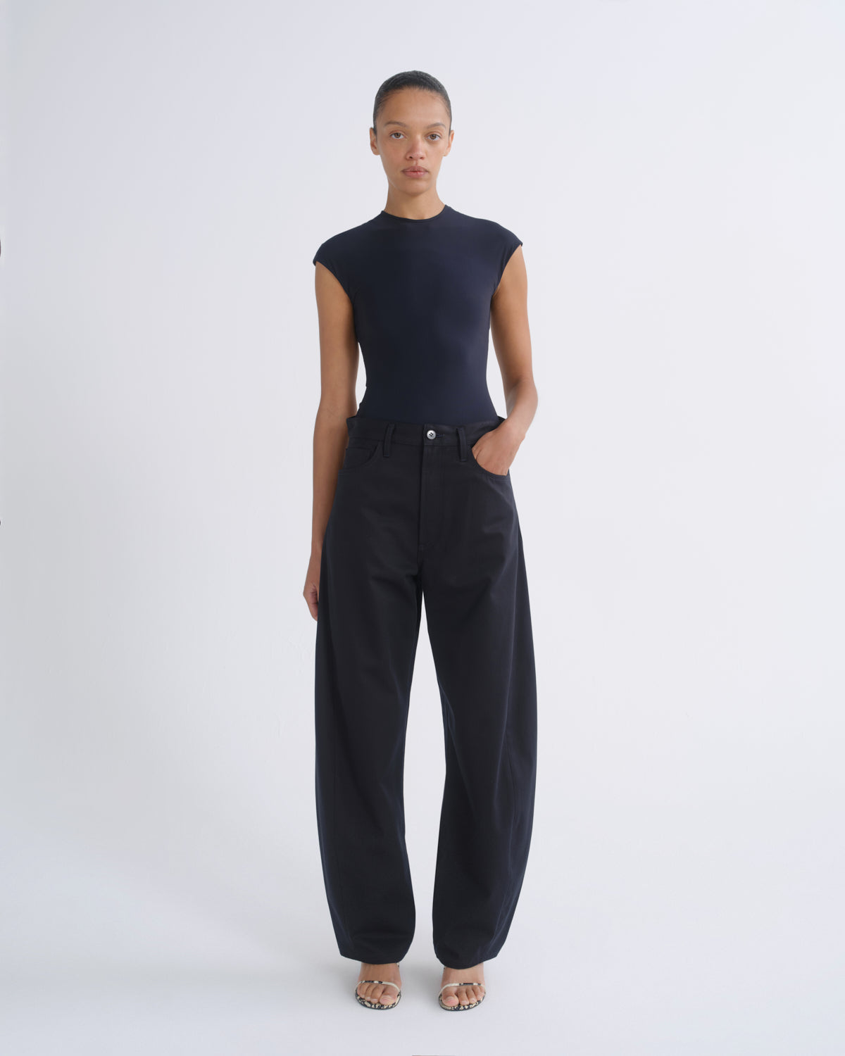 A model stands against a light gray studio background wearing a dark navy sleeveless mock-neck top and matching dark navy wide-leg pants.