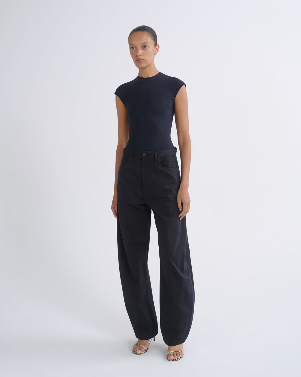 A model stands against a light gray studio background wearing a dark navy sleeveless top and matching dark navy wide-leg trousers.