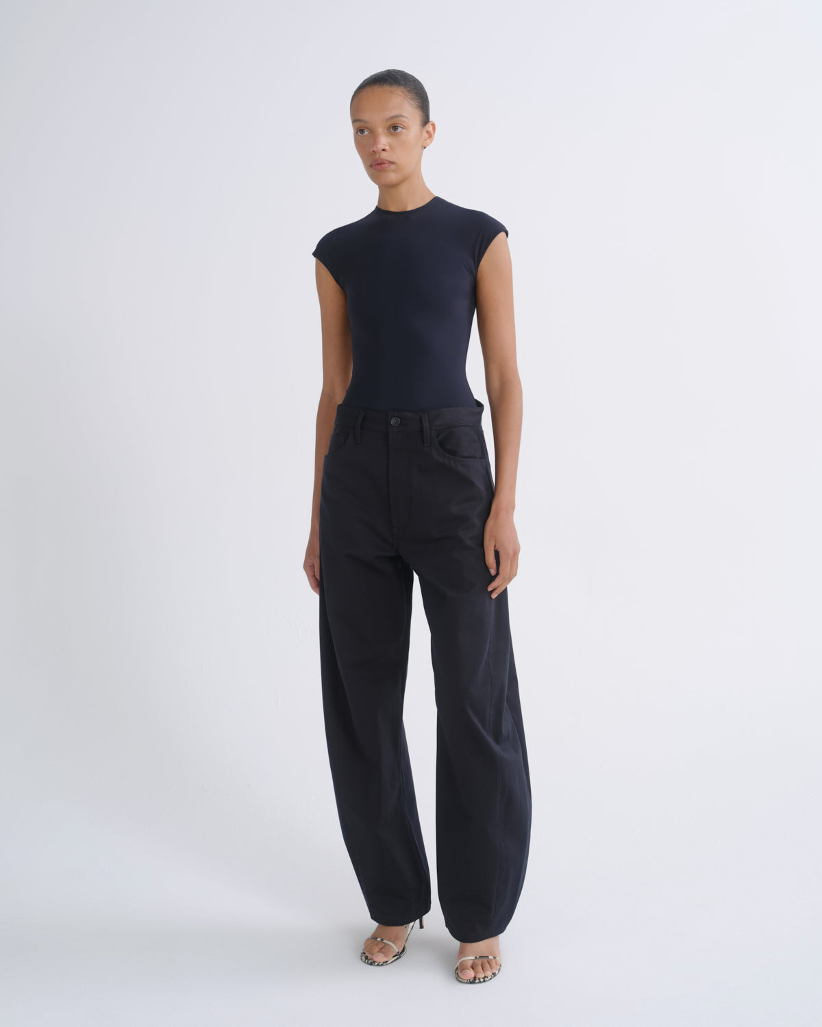 A model stands against a light gray studio background wearing a dark navy sleeveless top and matching dark navy wide-leg trousers.