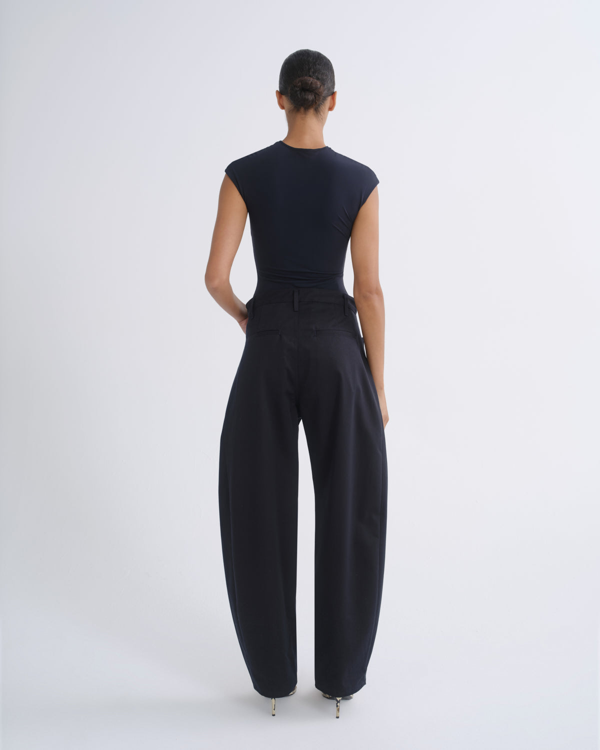 A model shown from the back wearing a dark navy sleeveless top and matching dark navy wide-leg trousers, standing against a light gray studio background.