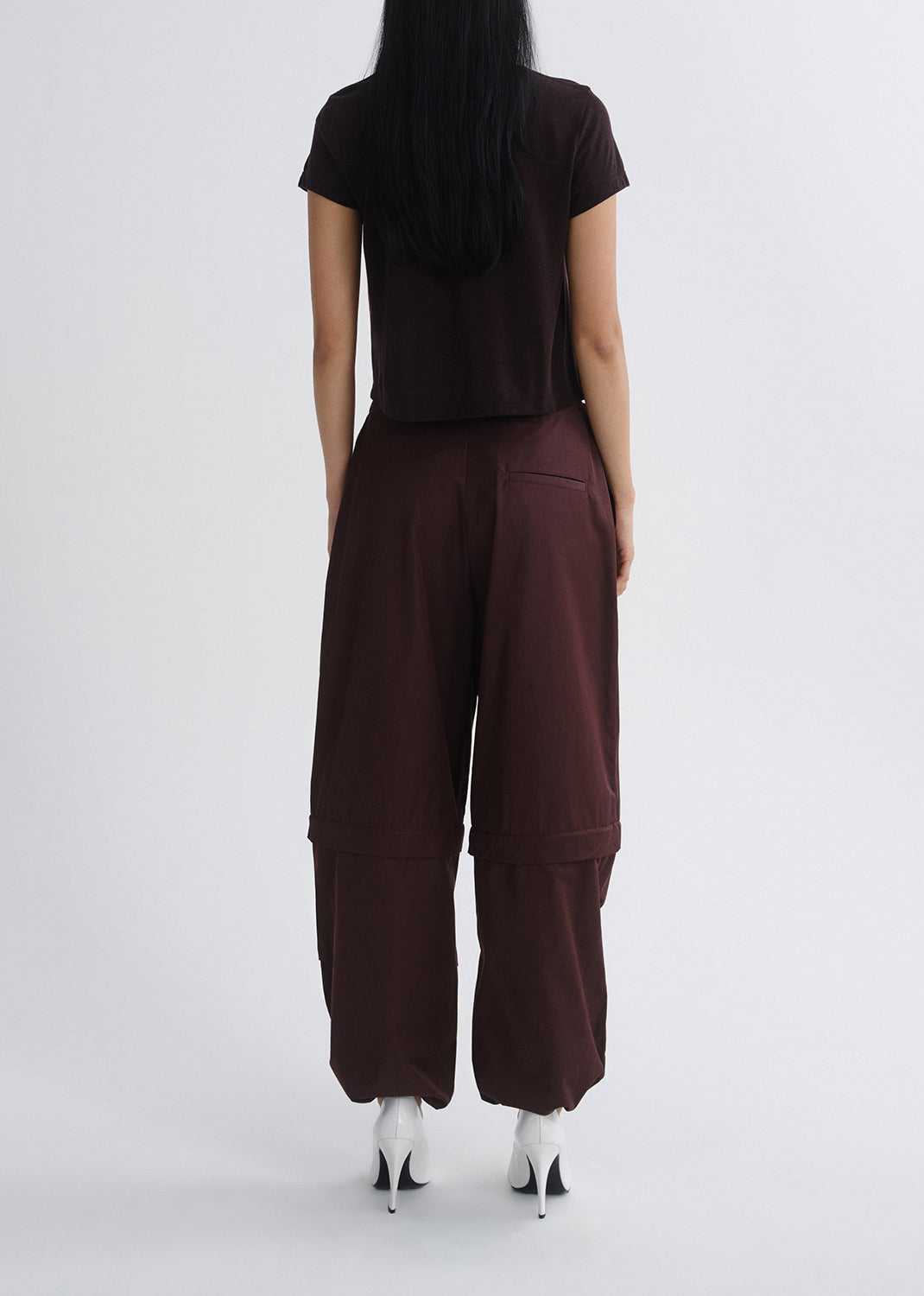 Person wearing a dark brown outfit with wide-leg pants on a grey background