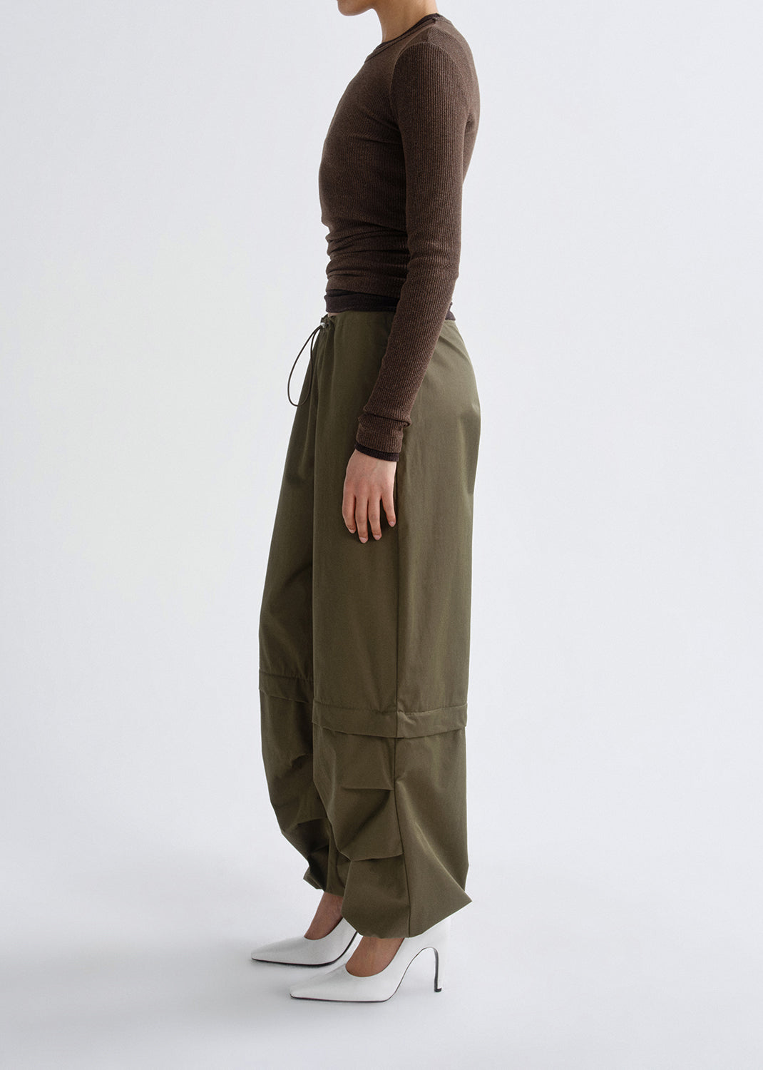 Person wearing olive green cargo pants and a brown top on a grey background
