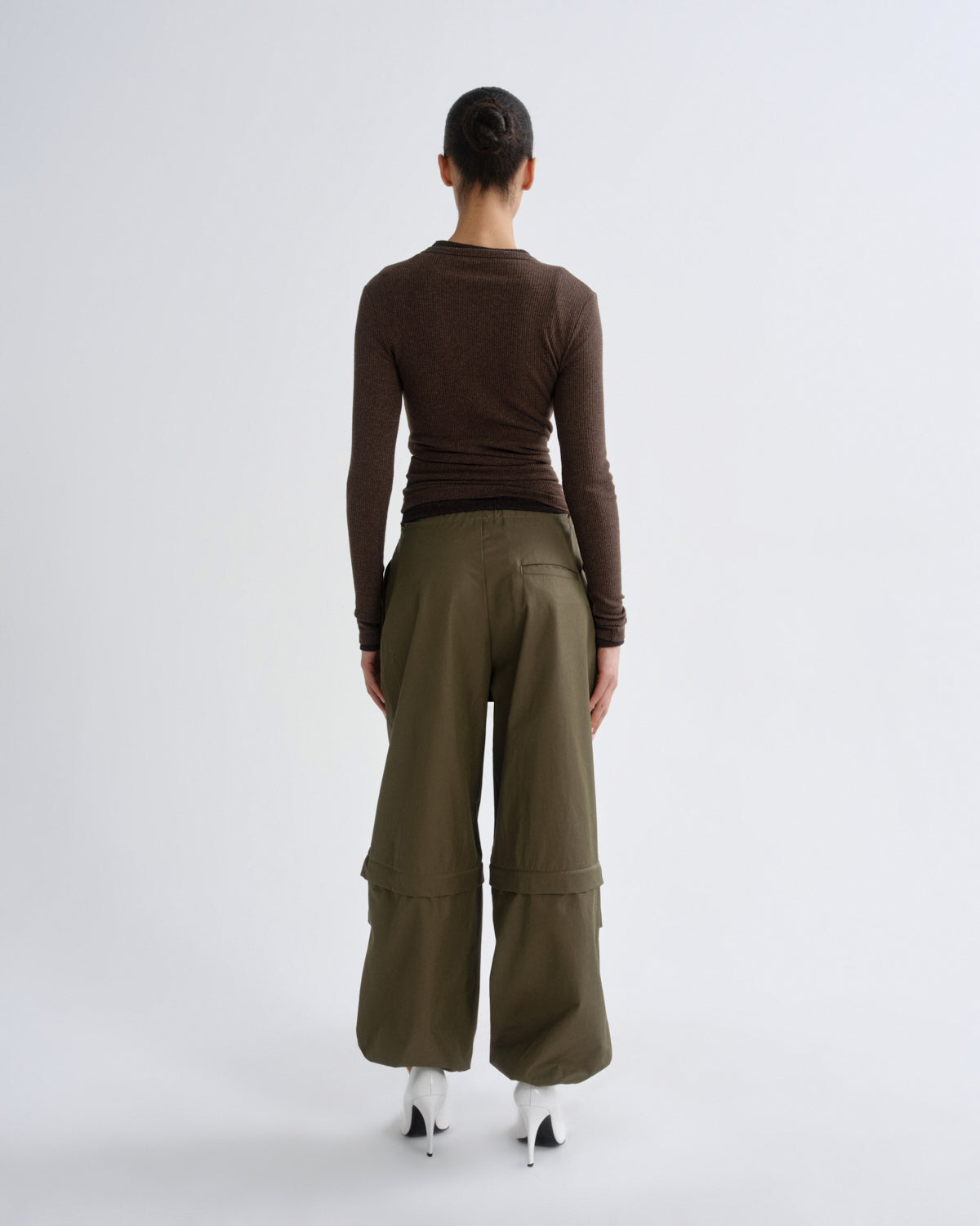 A model shown from the back wearing a dark brown long-sleeve top and olive green wide-leg cargo pants, standing against a light gray studio background.