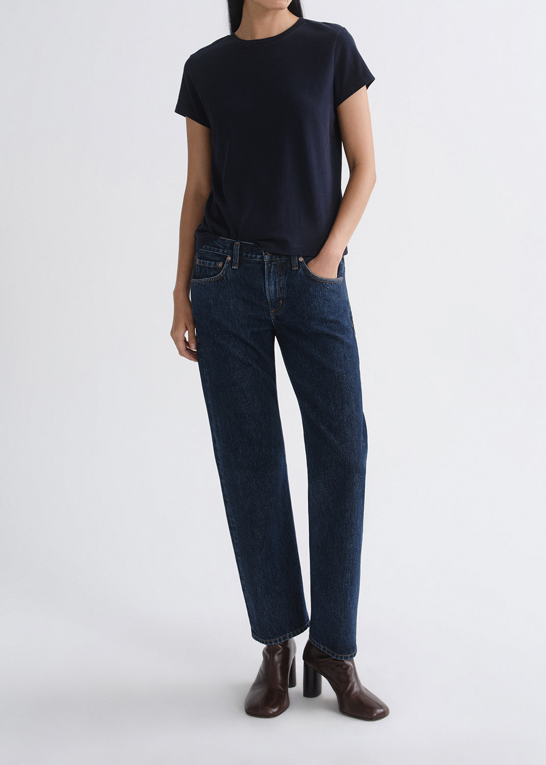 Person wearing a black t-shirt and dark blue jeans on a grey background