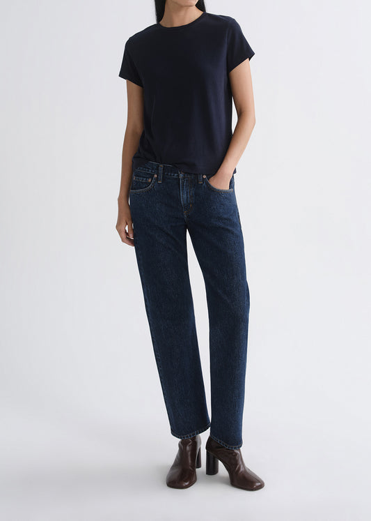 Person wearing a black t-shirt and dark blue jeans on a grey background