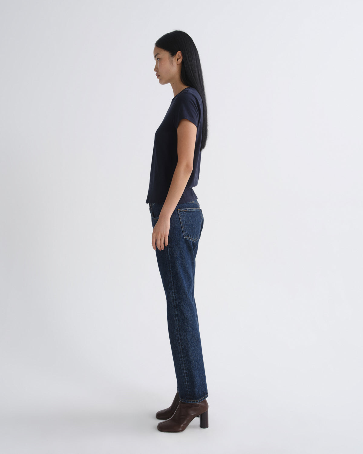 Woman wearing a dark blue t-shirt and jeans standing against a white background