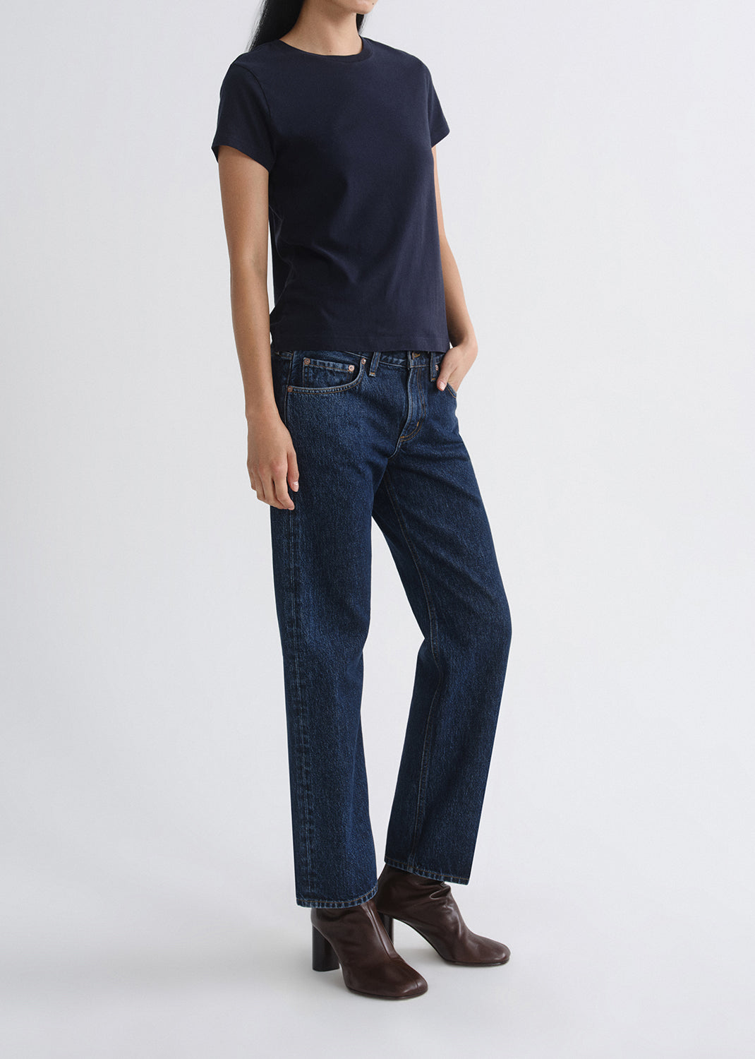 Person wearing a navy t-shirt and dark blue jeans on a grey background