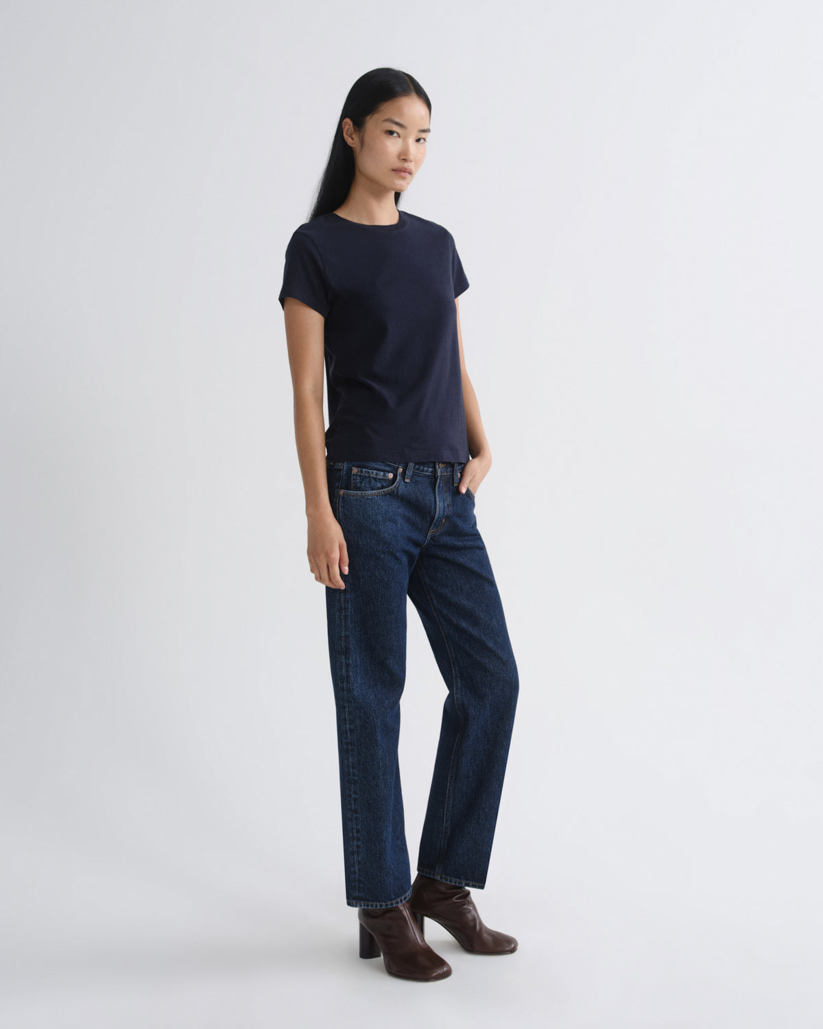 Person wearing a navy t-shirt and dark blue jeans on a white background