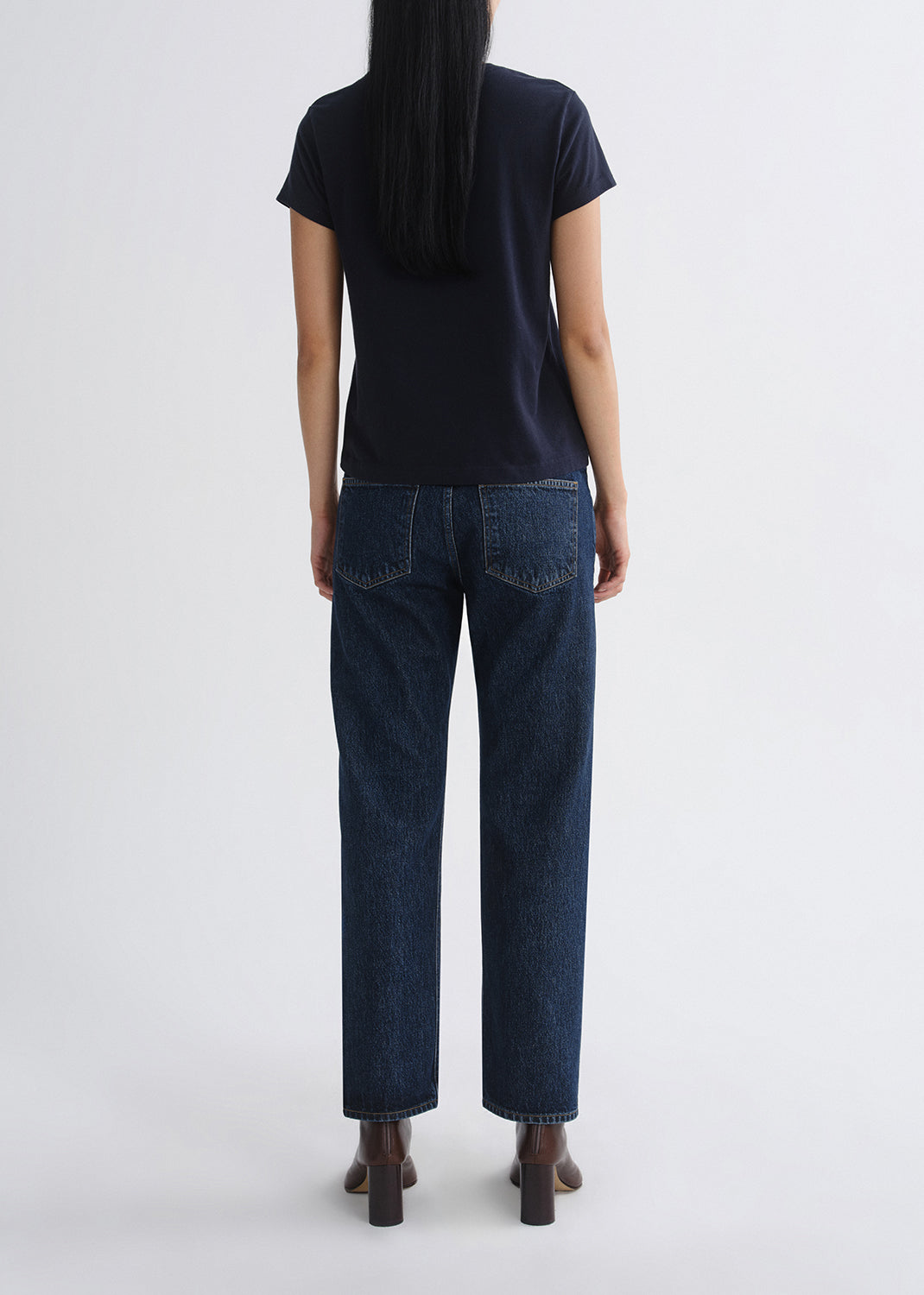 Person wearing a black t-shirt and dark blue jeans from behind on a grey background