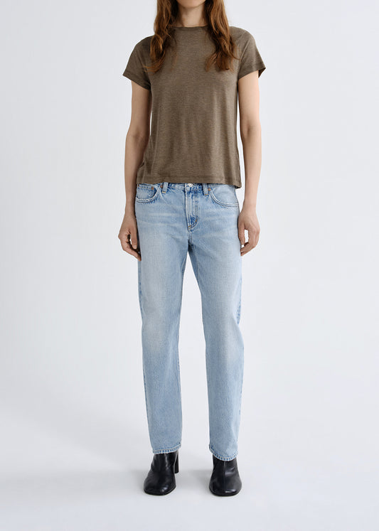 Person wearing a brown t-shirt and light blue jeans on a grey background