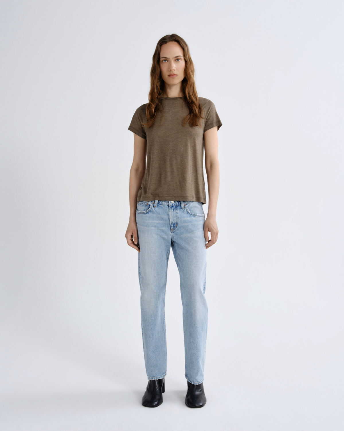 Woman wearing a brown t-shirt and light blue jeans on a white background