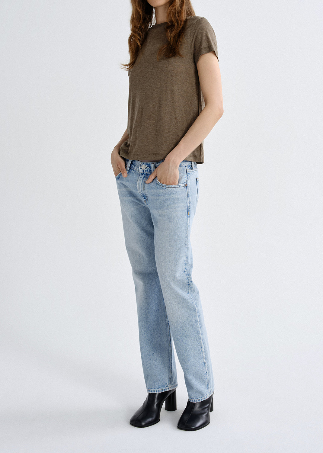 Person wearing a brown t-shirt and light blue jeans on a grey background
