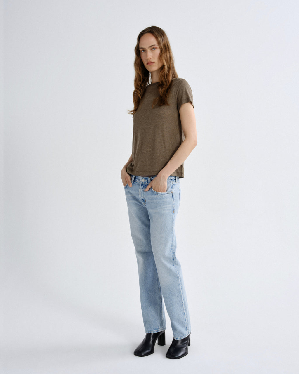 Woman wearing a brown t-shirt and light blue jeans on a white background