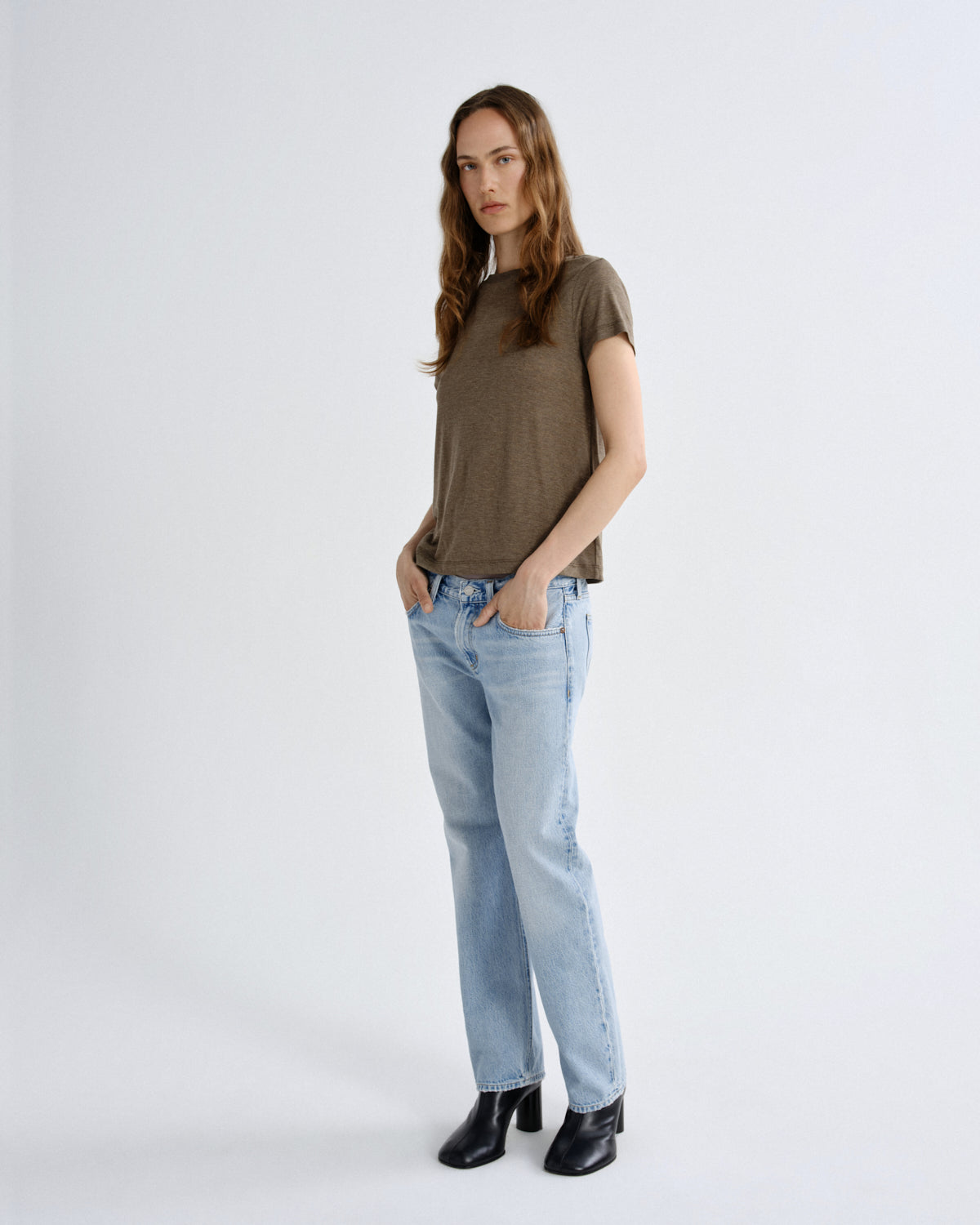 Woman wearing a brown t-shirt and light blue jeans on a white background