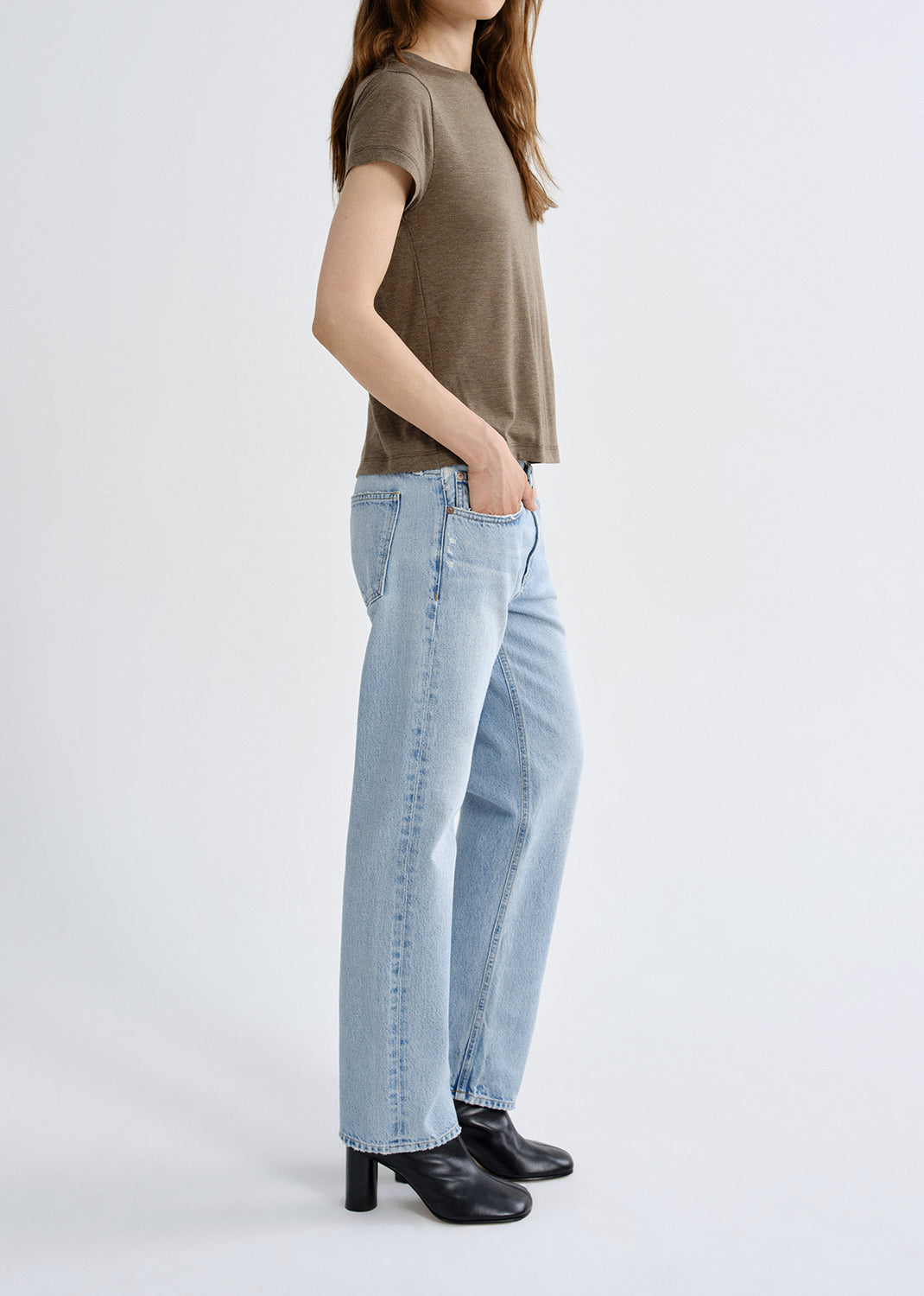 Person wearing a green t-shirt and light blue jeans on a grey background