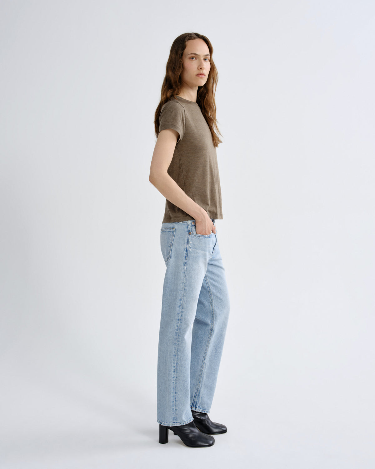Woman wearing a brown t-shirt and light blue jeans on a white background