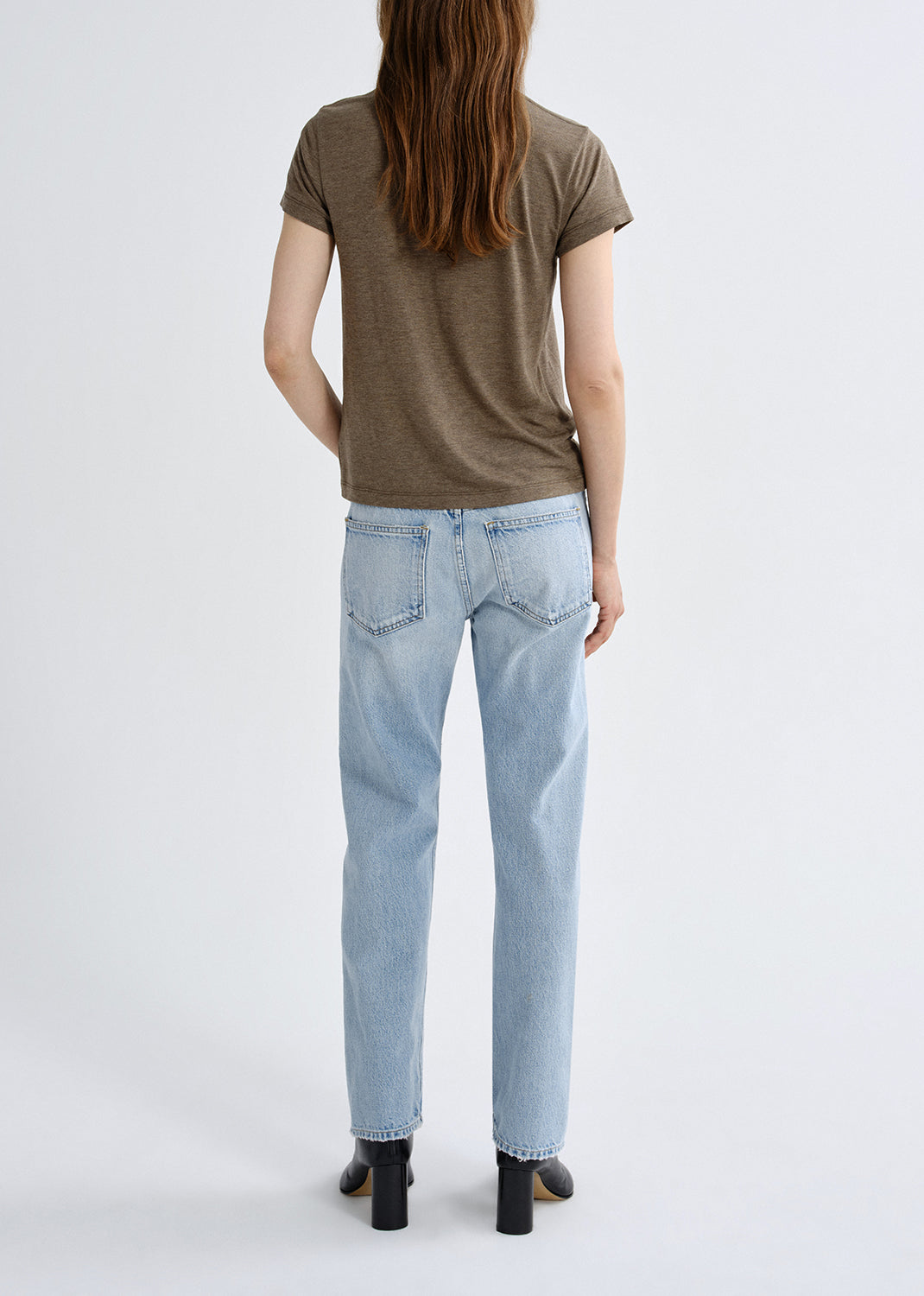 Person wearing a brown t-shirt and light blue jeans on a grey background