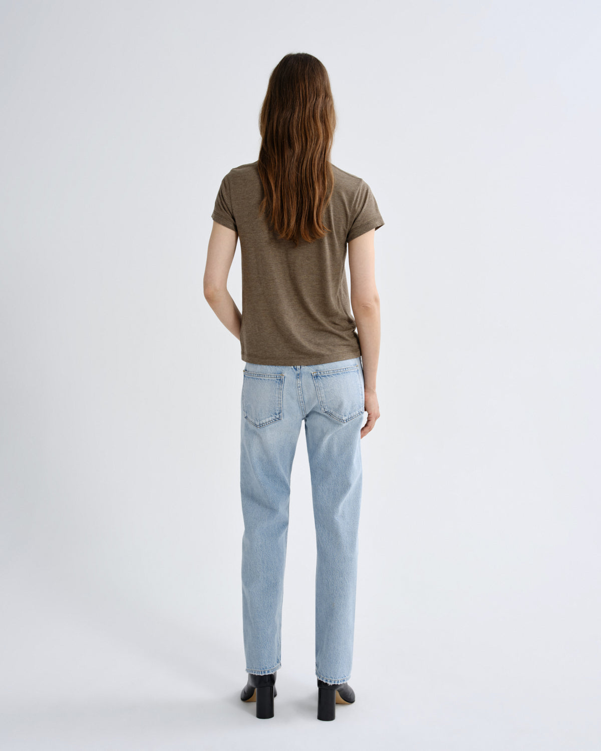 Person wearing a brown t-shirt and light blue jeans on a white background