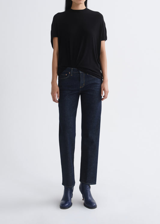 A model wearing a black short-sleeve t-shirt, dark blue straight-leg jeans, and dark blue leather ankle boots, standing against a grey background.
