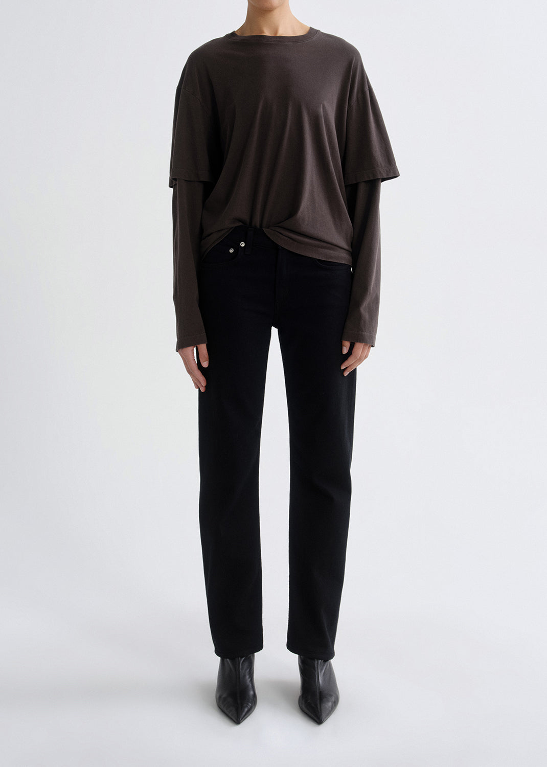 Person wearing a brown long-sleeve top and black pants on a grey background