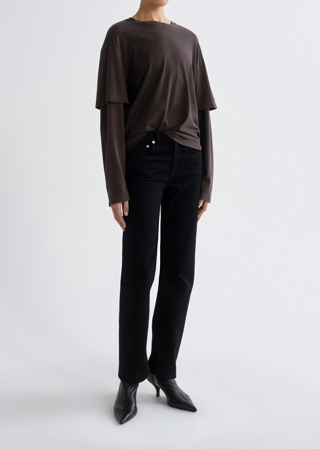 Person wearing a brown long-sleeve top and black pants on a grey background
