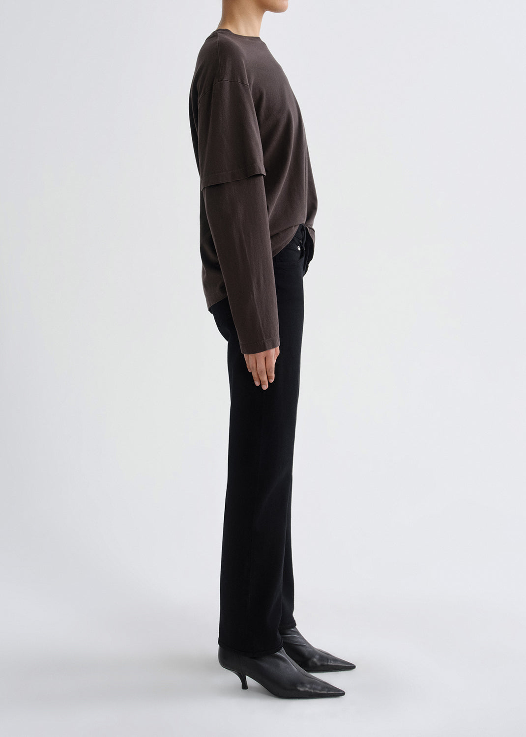 Person wearing a brown sweater and black pants on a grey background