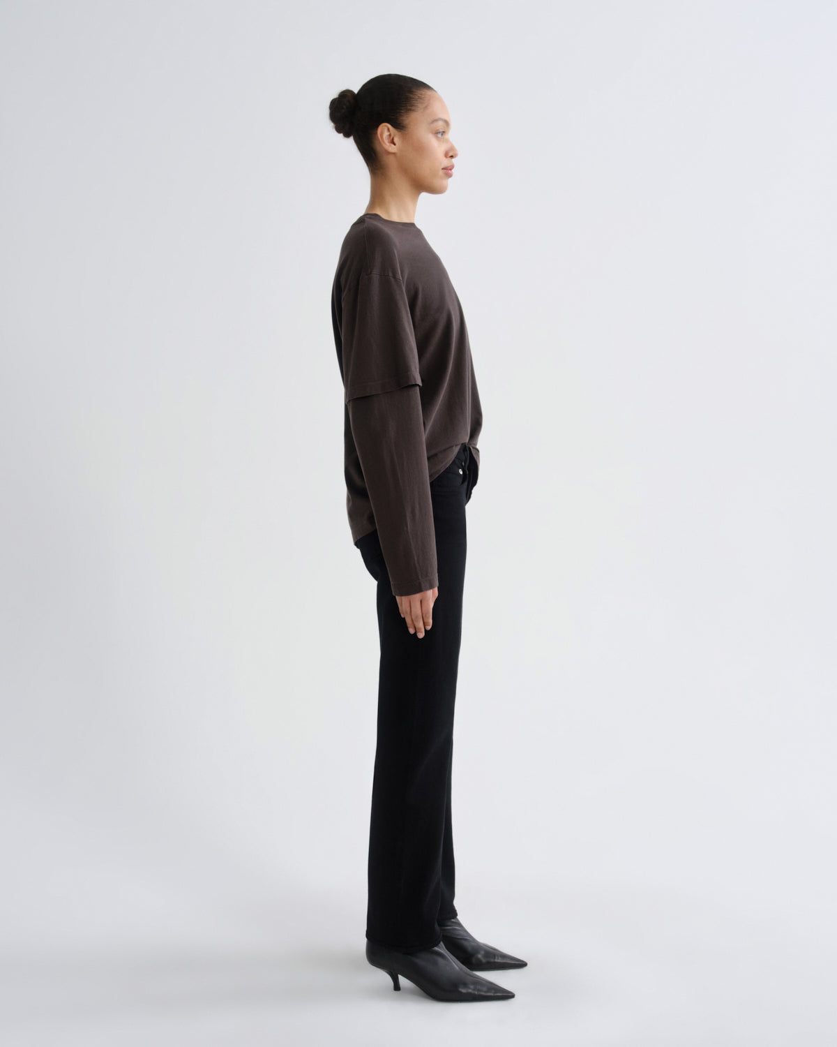 Person wearing a brown sweater and black pants on a white background