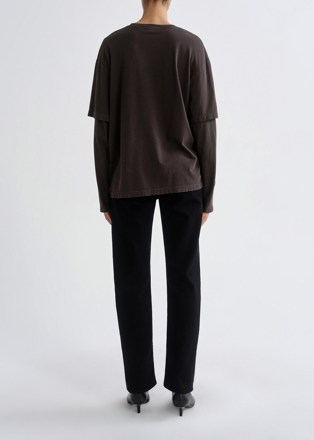Person wearing a dark brown long-sleeve top and black pants on a grey background